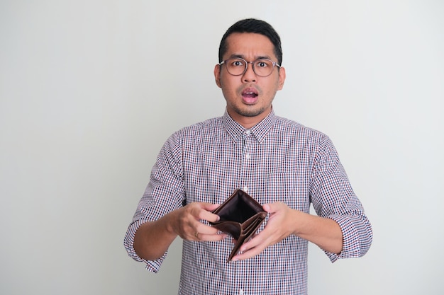 Adult Asian man showing his empty wallet with worried expression