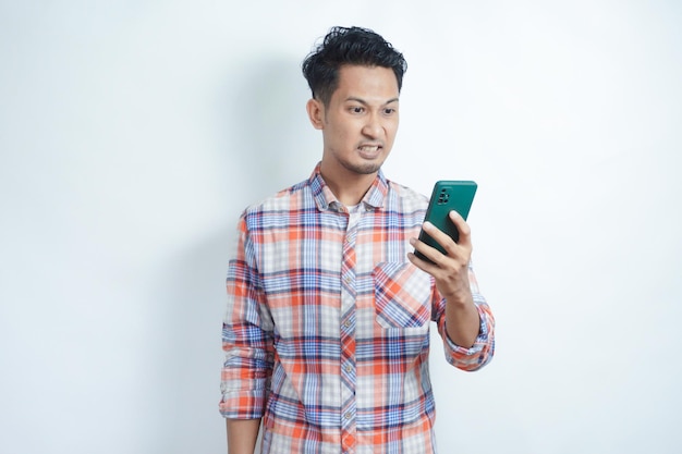 アジア人の成人男性が携帯電話を見ているとき怒りの表情を示しています