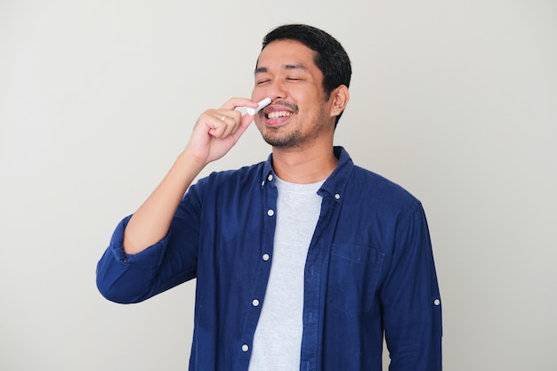 Adult Asian man showing relieved expression when using nasal stick inhaler