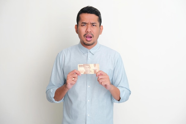 Photo adult asian man showing sad expression while holding small amount of money