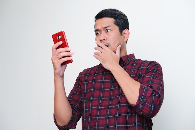 Photo adult asian man showing shocked expression when looking to his mobile phone