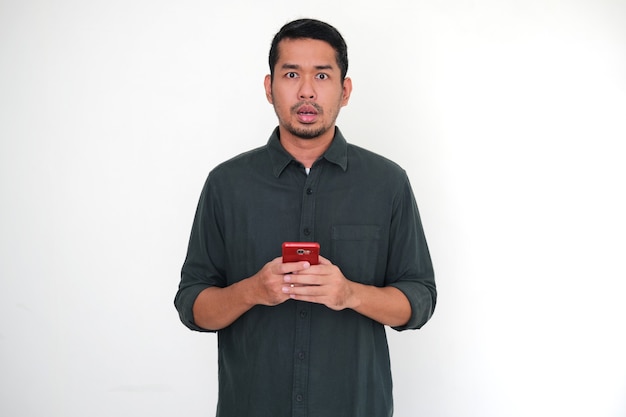 Adult Asian man showing shocked face expression when holding his mobile phone