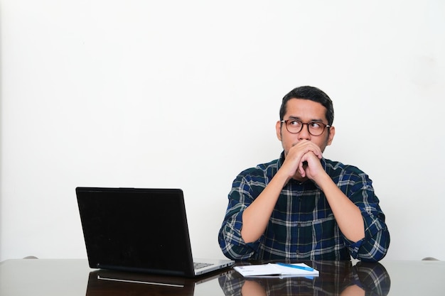 Adult Asian man sitting in his working desk showing thinking pose