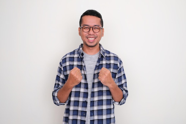 Adult Asian man smiling at the camera and clenching both hands showing excitement