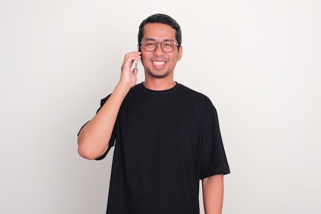 Photo adult asian man smiling at the camera while calling using mobile phone