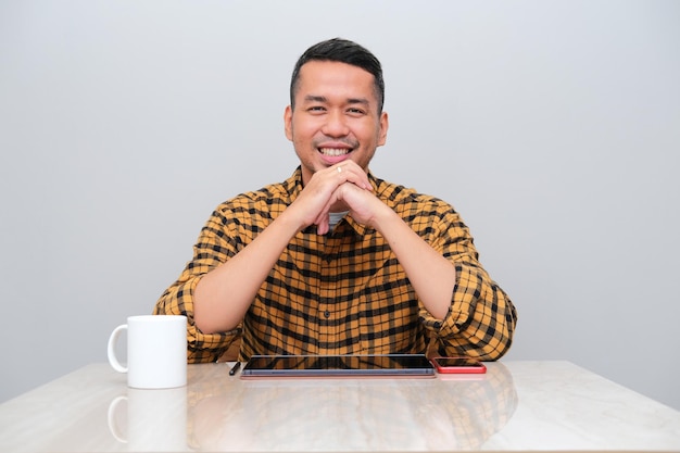 Adult Asian man smiling confident with his gadget stuff placed above the table