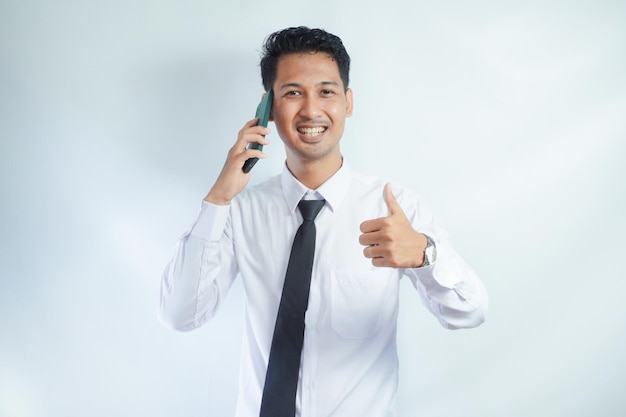 Photo adult asian man smiling and give thumb up while answering a phone call