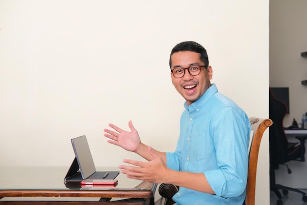 Adult Asian man smiling happy when sitting in front of his mobile tablet