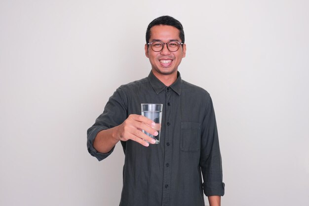 Adult Asian man smiling happy while offering a glass of water