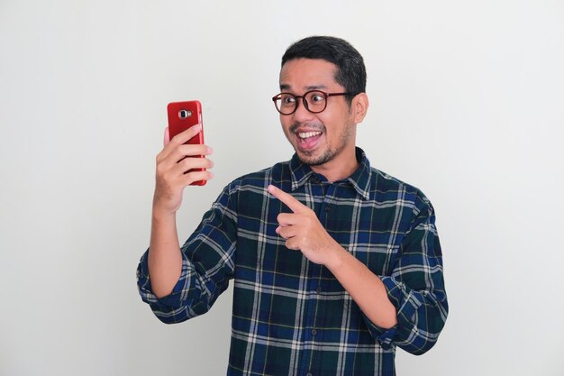 Photo adult asian man smiling happy while pointing to mobile phone that he hold