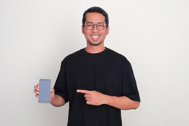 Adult Asian man smiling happy with one hand pointing at blank phone screen that he hold