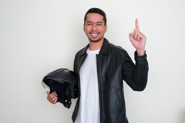 Adult Asian man smiling and pointing finger up while holding a motorcyle helmet