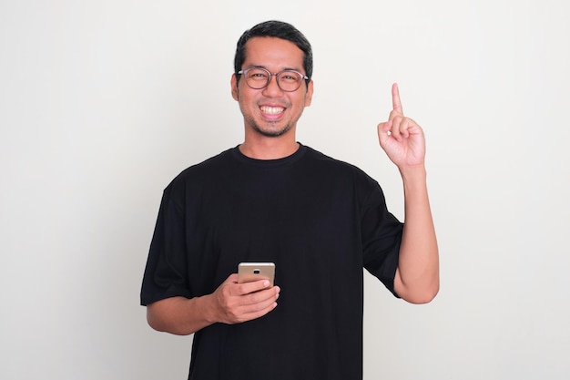 Adult Asian man smiling and pointing one hand up while holding mobile phone