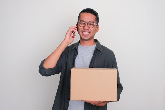 Photo adult asian man smiling when calling and holding a package box