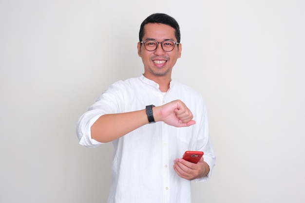 Adult Asian man smiling while holding mobile phone and showing his watch