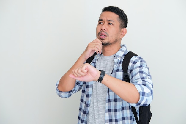 Adult Asian man wearing backpack waiting for someone to pick him up with unsure expression