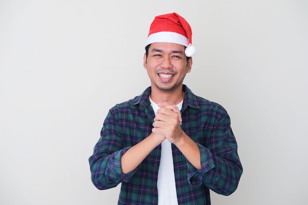 Adult Asian man wearing christmas hat smiling while showing friendship hand gesture