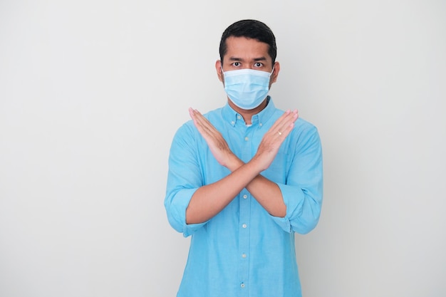 Взрослый азиатский мужчина в медицинской маске показывает серьезное выражение лица и показывает рукой знак "стоп"