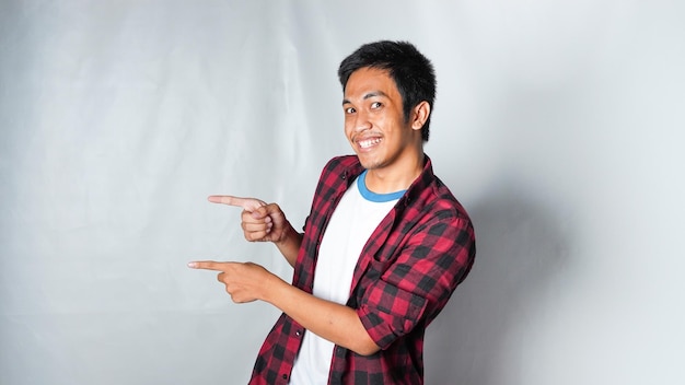 Photo adult asian man wearing red flannel tshirt pointing left area with smiling face isolated white background