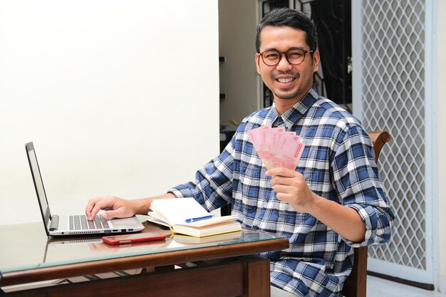 Photo adult asian man working in the table and showing paper money