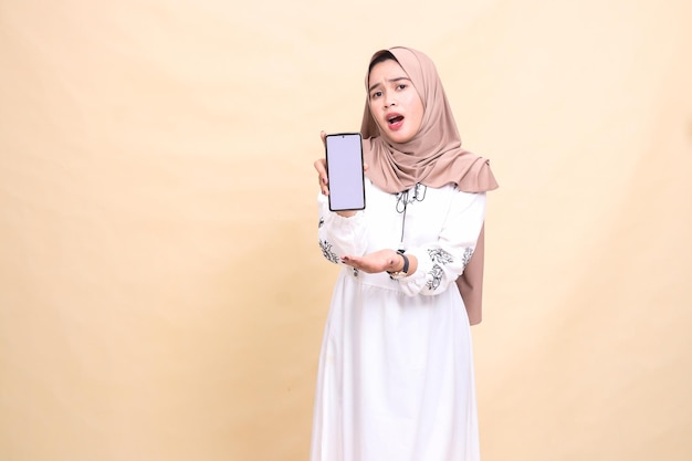 an adult Asian Muslim woman wearing a hijab is shocked to display a cellphone screen gadget to creat