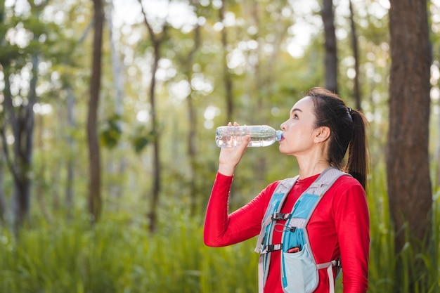 La donna asiatica adulta trail runner con giubbotto da corsa beve acqua durante la pausa di allenamento per il trail running nel parco forestale