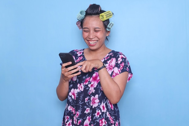 Adult asian woman wear colorful hair rollers laughing while looking at smartphone