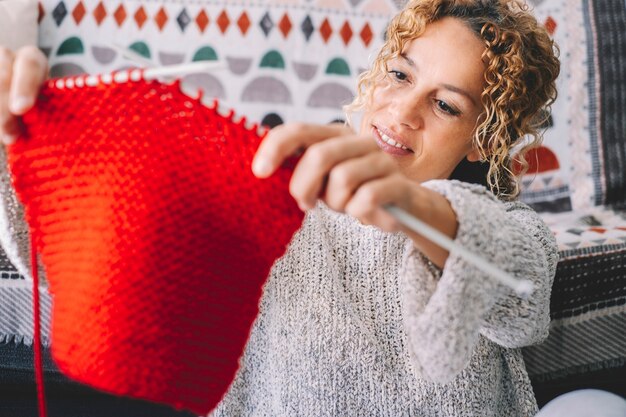 Donna attraente adulta a casa in attività di lavoro a maglia utilizzando lana colorata. gente femminile felice e rilassata che si gode il tempo al coperto sul divano. lavoro a maglia