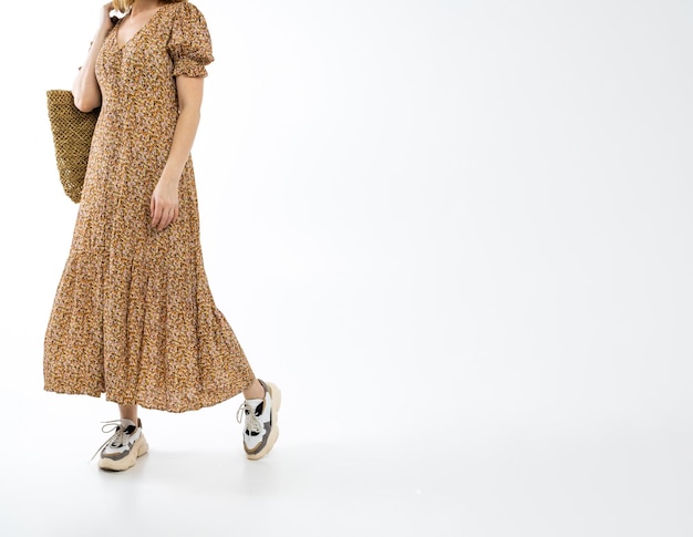 Adult attractive woman in a long brown dress with a brown wicker bag and sneakers on a white background