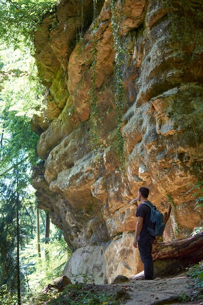 An adult backpacker walking around a cave in a forest on a sunny day