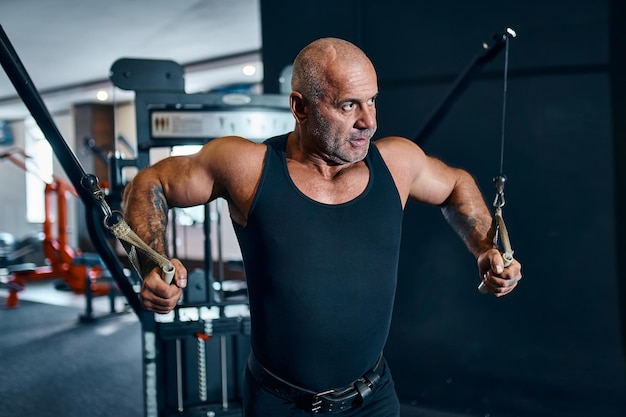 adult bald man bodybuilder in the gym during training who is an athlete trainer or instructor