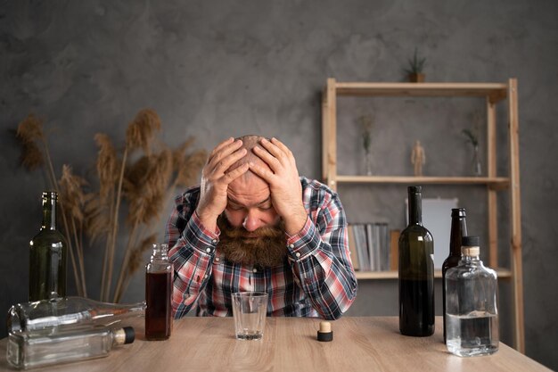 사진 집에서 술 한 병을 마시는 테이블에 앉아있는 성인 수염 남성 슬픈 혼자 알코올 중독