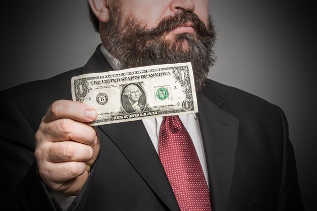 Adult bearded man in a suit holding a dollar