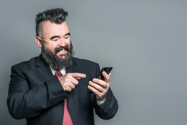 Adult bearded man in a suit holding a phone on a gray background