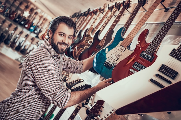 Adult bearded musician buys electric guitar in music store.