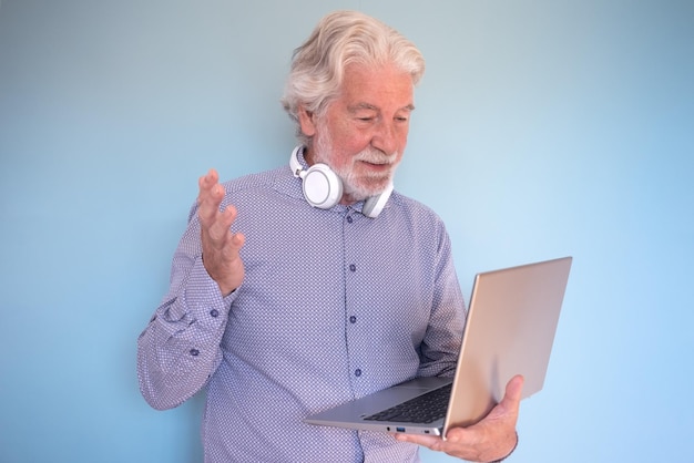 온라인 연결 작업을 하는 헤드폰을 끼고 화상 채팅을 하는 동안 노트북을 들고 있는 수염 난 노인 사업가 70세