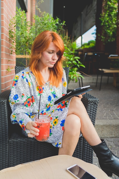 Adult beautiful woman sitting outdoor having drink using tablet