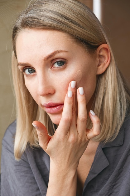 Adult blond woman touching cheek enjoying perfect face looking in mirror Daily routine