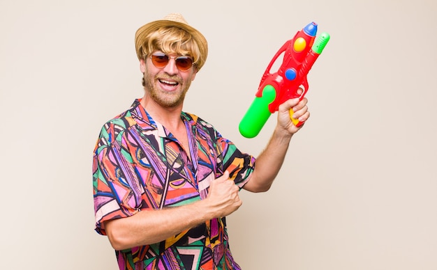 Adult blonde man on holidays holding a water gun.