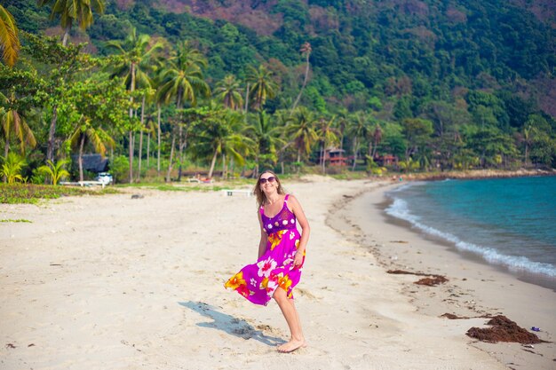 An adult blonde woman in a bright dress on a tropical seashore laughs. Travel and tourism.