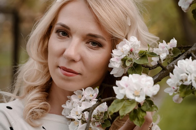 Портрет взрослой блондинки, наслаждающейся цветущим деревом в весеннем саду