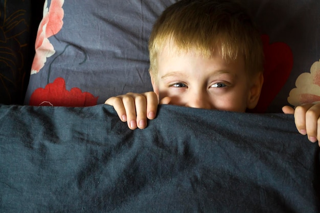 An adult boy peeks out from under the blanket