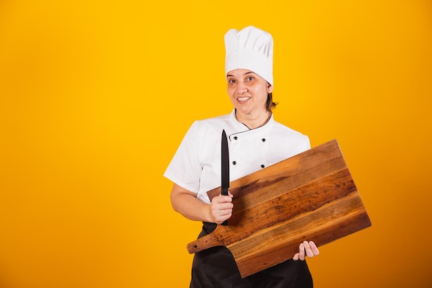 Adult Brazilian woman chef master in gastronomy holding wooden chopping board and knife
