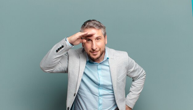 Adult businessman looking bewildered and astonished, with hand over forehead looking far away, watching or searching