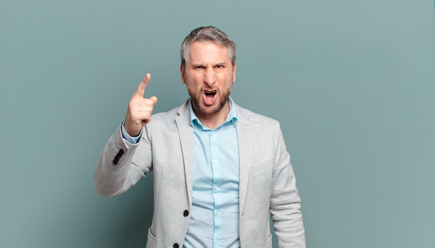 Adult businessman pointing with an angry aggressive expression looking like a furious, crazy boss