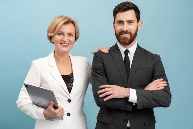 Photo adult businessman and senior businesswoman wearing formal suits holding laptop posing with pleasure smiles isolated over blue background