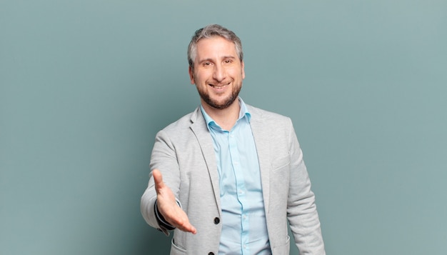 Adult businessman smiling, looking happy, confident and friendly, offering a handshake to close a deal, cooperating