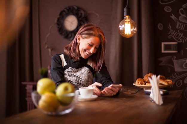 Donna di affari adulta che ride mentre guarda il suo telefono. ricreazione in una caffetteria vintage