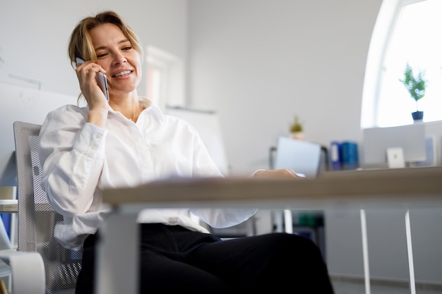 Adult businesswoman in white shirt talking on mobile phone in office