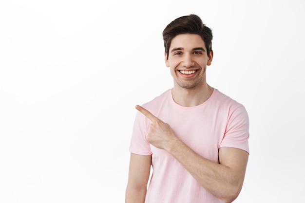 Adult candid caucasian man smiles and points aside, shows copy spaces, way to your logo, standing over white background